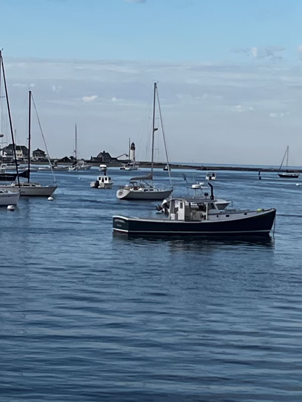 A working boat on its mooring in Scituate Harbor, the lighthouse on the point behind